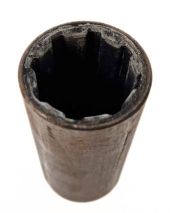 Nahaufnahme einer abgenutzten, schwarzen, zylindrischen Büchse mit Gummi 100/24 mit zwölfzackigem Innenleben, isoliert auf weißem Hintergrund.