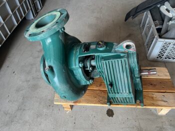 Die Caprari-Pumpe MEC-D 03/100A, eine große grüne Industriepumpe mit sichtbarem Flansch und Motorgehäuse, steht auf einer Holzpalette auf einem Betonboden.