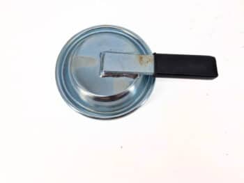 Die Endkappe mit Hebel HK108, ein kleiner Topfdeckel aus Metall mit einem schwarzen Kunststoffgriff, wird auf eine weiße Fläche gelegt.