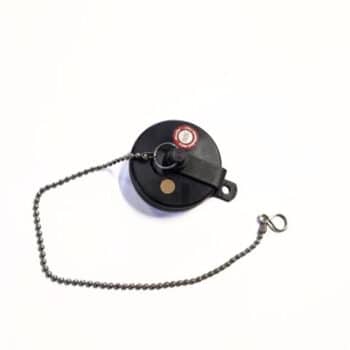 Ein "Tankdeckel alt", ein schwarzer runder Gegenstand mit einer kleinen Kette und einer Metallschlaufe, ist vor einem weißen Hintergrund zu sehen.