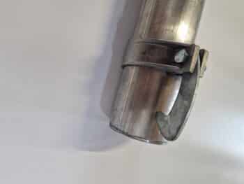 Das Regnerpassrohr Aluminium 102/50 cm mit angebauter Schelle und Bolzen wird schräg auf eine schlichte helle Fläche gelegt.