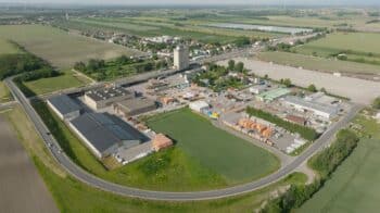 Luftaufnahme eines Industriekomplexes, der verschiedene Dienstleistungen anbietet, mit mehreren Gebäuden, Lagerflächen und Parkplätzen, die von Feldern umgeben sind und von Straßen durchschnitten werden.