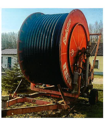 Eine Bauer Rainstar 90/430m Schlauchtrommel mit schwarzem Schlauch ist auf einem Metallgestell mit Rädern montiert und wird im Freien in der Nähe von Häusern und Bäumen aufgestellt.