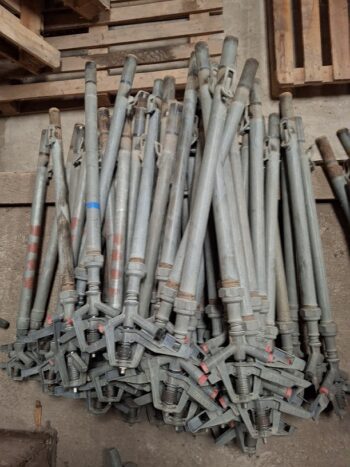 Ein Stapel verstellbarer Stahlgerüstböcke, gestapelt auf einem Betonboden, mit Holzpaletten im Hintergrund.