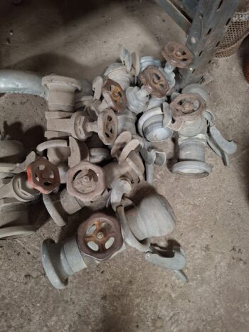 Ein Haufen staubiger, unbenutzter Industrieventile mit Handrädern und Hebeln, die auf einem Betonboden liegen.
