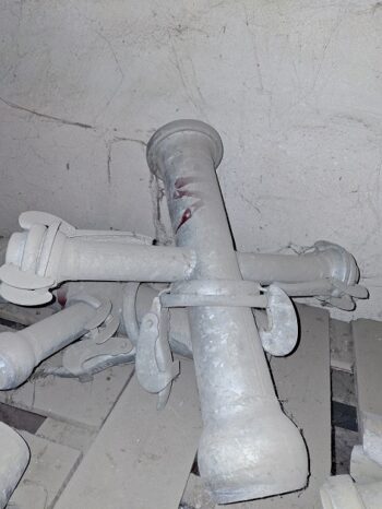 Drei verstaubte Rohrverbinder mit Riegeln liegen auf einem schmutzigen Boden vor einer rauen, fleckigen Wand.