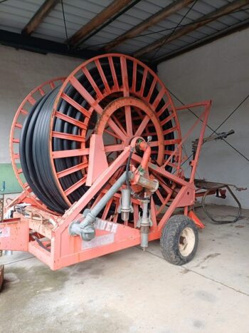 Rainstar Typ 82-360 S landwirtschaftliche Bewässerungstrommel mit schwarzem Schlauch auf rotem Metallrahmen, auf Rädern in einem Schuppen mit Betonboden.