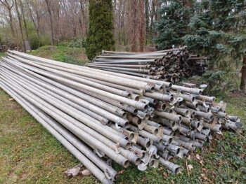 Im Freien sind die Stapel von Vielfalt und Beregnungsteilen auf einer Wiese angeordnet, umgeben von Bäumen und üppigem Grün.