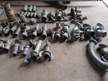 Vielfalt an Beregnungsteilen - verschiedene Metallrohrverschraubungen und -verbinder sind auf einer Betonfläche nach Typ und Größe sortiert ausgebreitet.